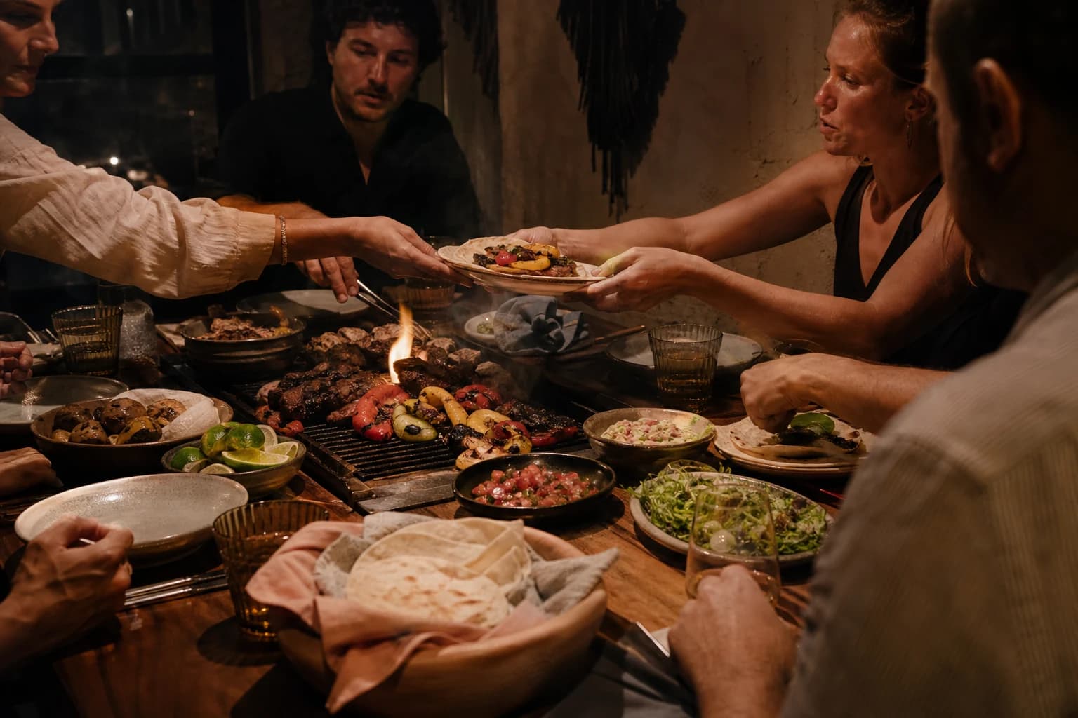 Friends sharing fajitas around Faji7a's live-fire table